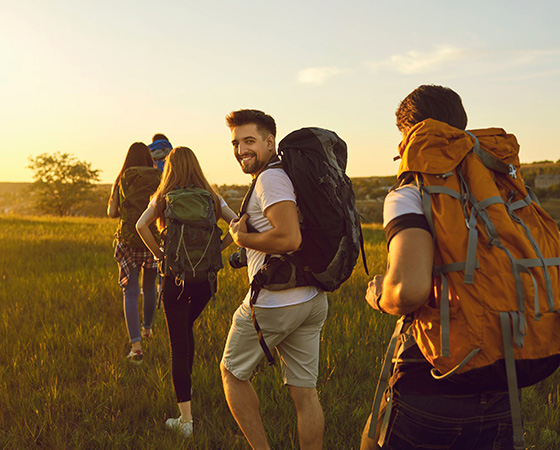 group of friends hiking in nature during sunset with backpacks and smiling faces enjoying outdoor adventure