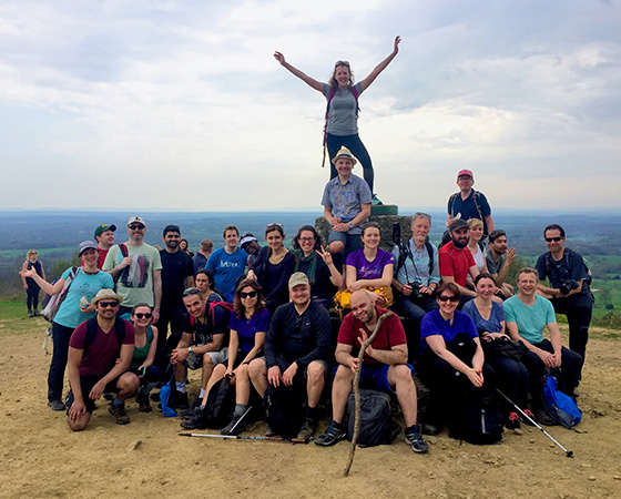 group of hikers celebrating on a mountain top during a hiking trip with two individuals posed atop a rock structure representing achievement and camaraderie