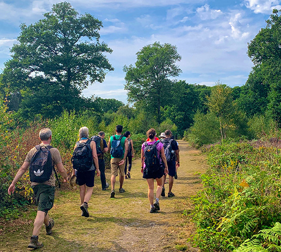 group of people hiking on a forest trail surrounded by greenery and trees enjoying nature and outdoor activity with two backpacks and two different clothing styles