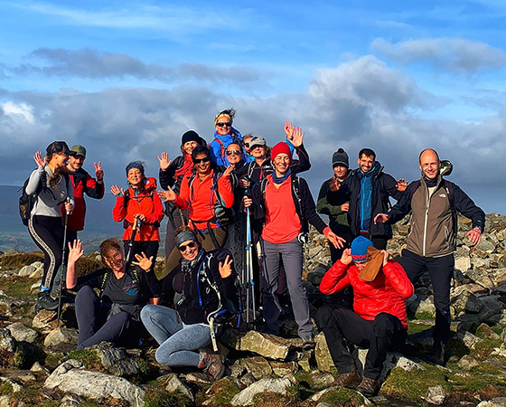 group of hikers celebrating on a rocky mountain peak with blue sky visible smiling and waving together on a sunny day team of five enjoying nature