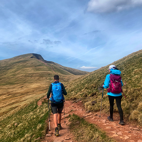 two hikers on a trail through green hills under a clear sky exploring nature for outdoor adventures